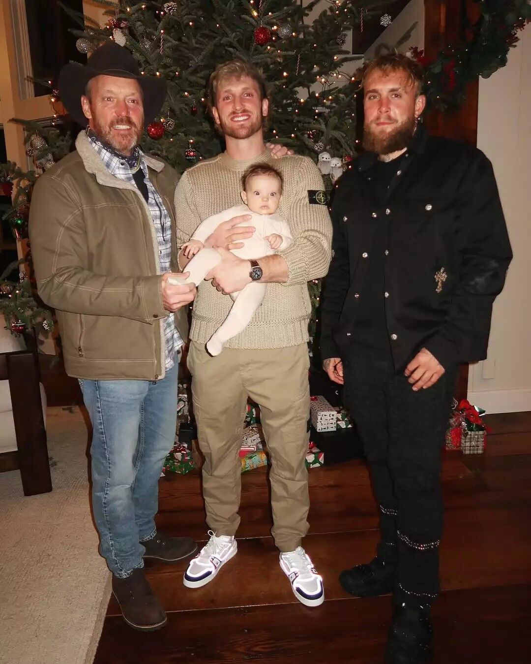 Logan paul carries his daughter as he poses for a photo with his father and his brother.