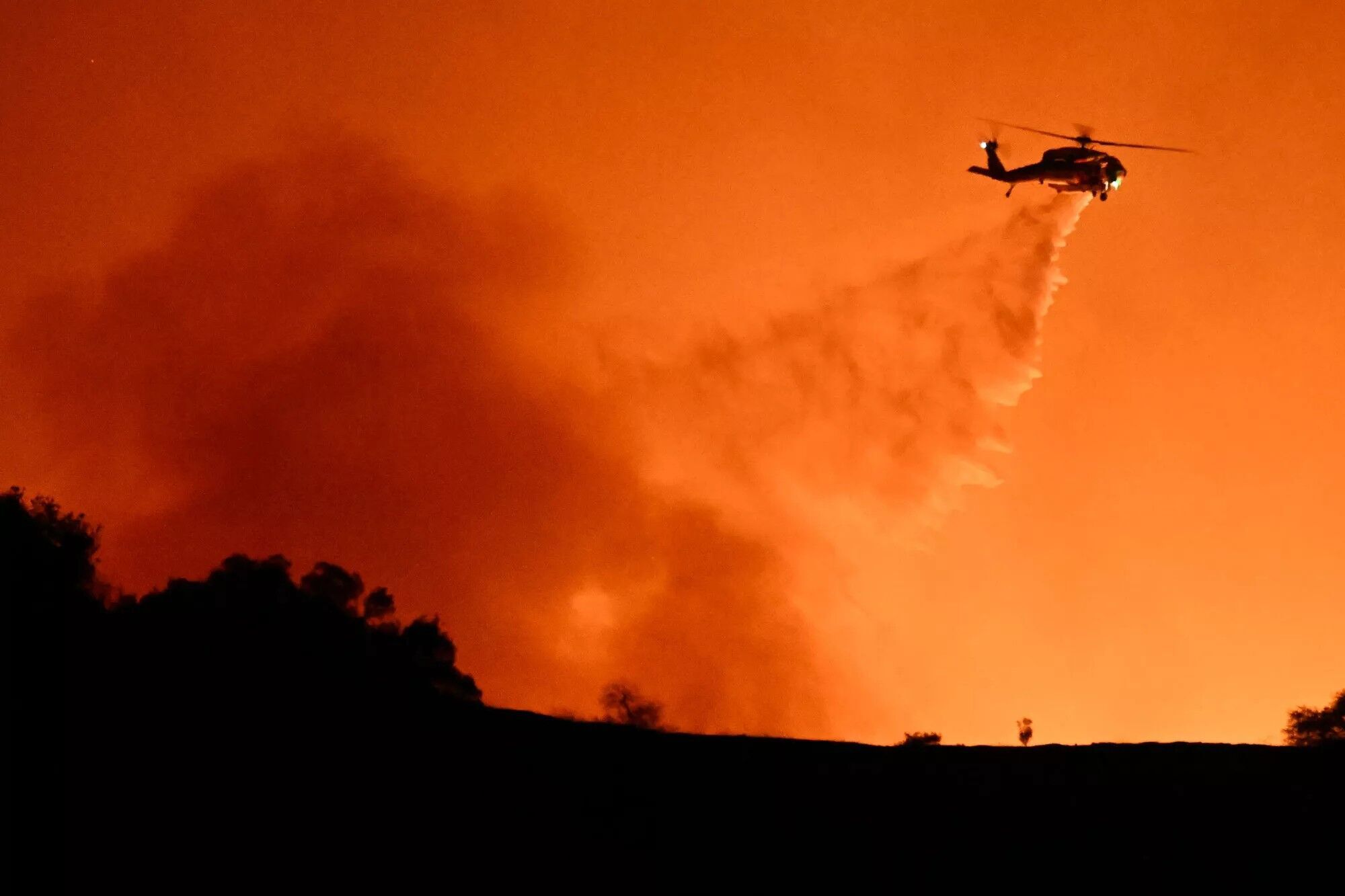 A helicopter drops water flames from the Palisades fire burning behind Mulholland drive in L.A. on Jan. 10