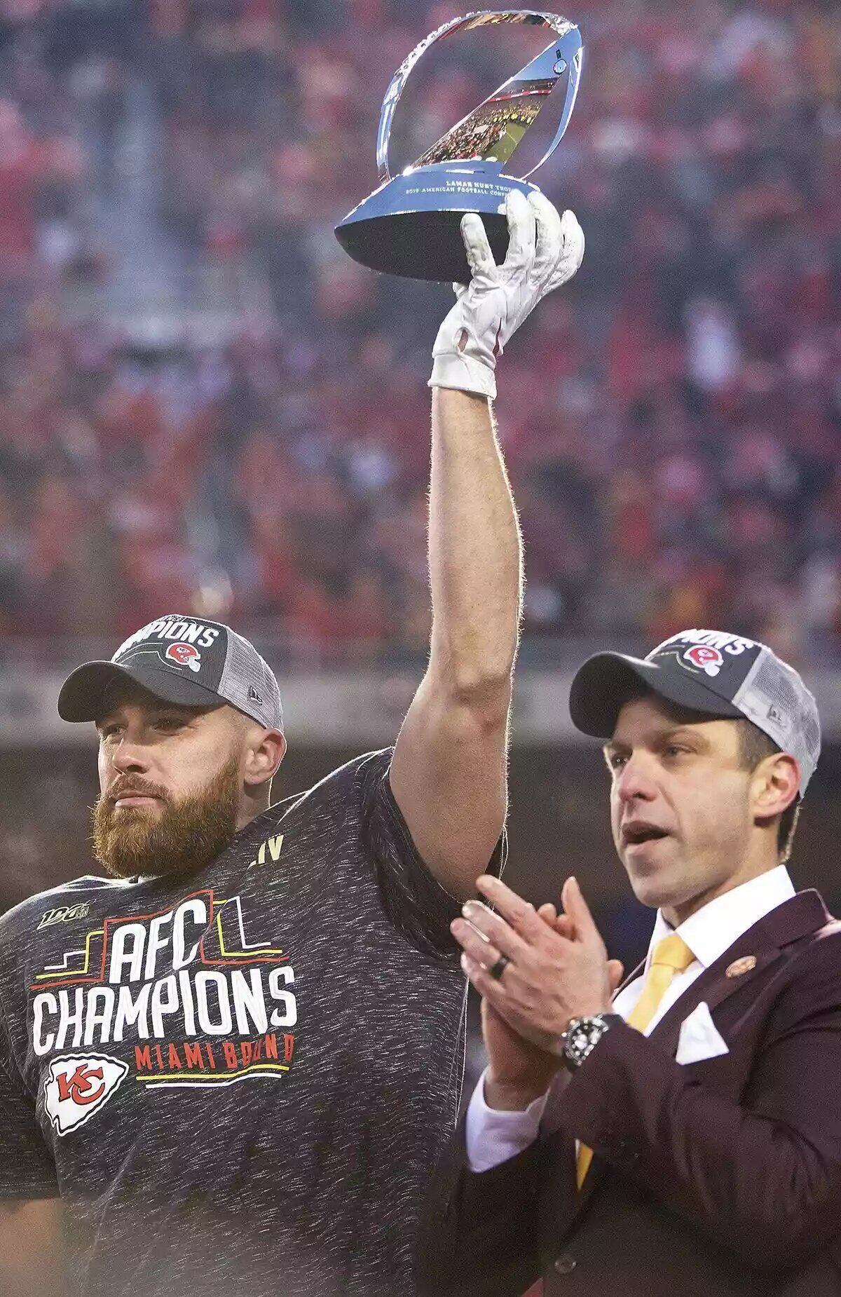 Kansas City Chiefs tight end Travis Kelce (87) holds the Lamar Hunt Trophy in the air as he stands on the trophy presentation stage next to Chiefs general manager Brett Veach after winning the game against the Tennessee Titans during the NFL AFC Championship football game.